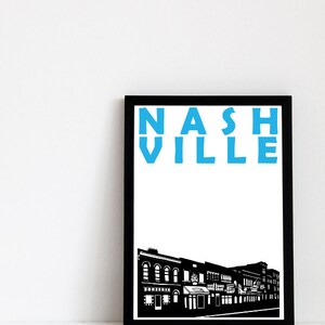 May include: Black and white framed print with a blue text overlay that reads "NASHVILLE". The print features a black and white silhouette of a city street with buildings.