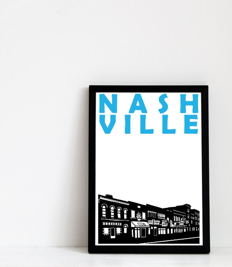 May include: Black and white framed print with a blue text overlay that reads "NASHVILLE". The print features a black and white silhouette of a city street with buildings.