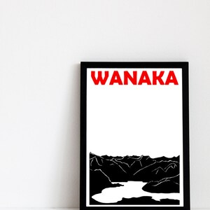 Puede incluir: Un cuadro enmarcado con la palabra "WANAKA" en letras rojas. Debajo, una ilustraci&oacute;n en blanco y negro de una cordillera y un lago. El cuadro est&aacute; en un marco negro.