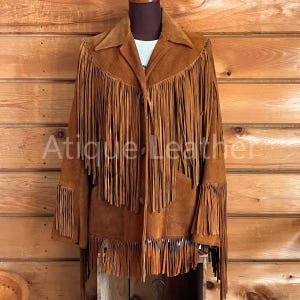 May include: A brown suede jacket with fringe detailing. The jacket has a button closure and two pockets.