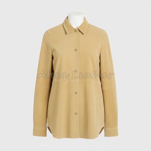 Puede incluir: Una camisa de ante color beige con mangas largas y cierre de botones. La camisa tiene un cuello clásico y se muestra en un maniquí. El texto "Ateeq Leather" es visible en la camisa.