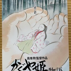 May include: A poster for the animated film "The Tale of the Princess Kaguya" features a watercolor illustration of a woman in a kimono held in cupped hands. The background shows a bamboo forest. Japanese text is visible.