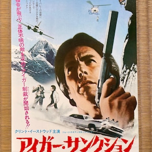 Puede incluir: Un cartel de película vintage de "The Eiger Sanction" con Clint Eastwood. El cartel tiene texto japonés e imágenes de un hombre sosteniendo un arma, un helicóptero y un coche. La paleta de colores incluye azules, blancos y marrones.