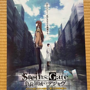 Peut inclure: Affiche promotionnelle pour le film d'animation "Steins;Gate: The Movie - Load Region of Déjà Vu". L'image présente deux personnages dans une rue de la ville. Le titre est en anglais et en japonais.