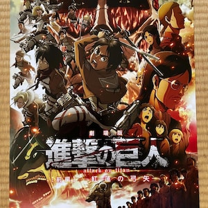 May include: A poster for the anime film "Attack on Titan" features a collage of characters in action, with a giant titan face dominating the background. Japanese text is visible, along with the film's title and a tagline.