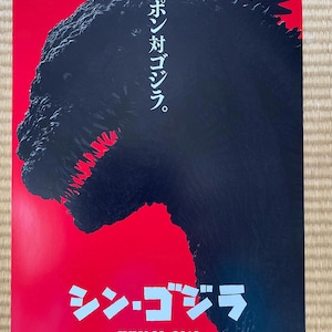 May include: A film poster in red and black, featuring a monster silhouette with visible teeth. Japanese text includes "シン・ゴジラ" and "JULY 29, 2016". The top text reads "ニッポン対ゴジラ".