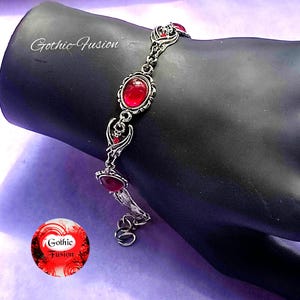 May include: A silver bracelet with a chain link design and red gemstone accents. The bracelet features a delicate, intricate design with a gothic aesthetic.