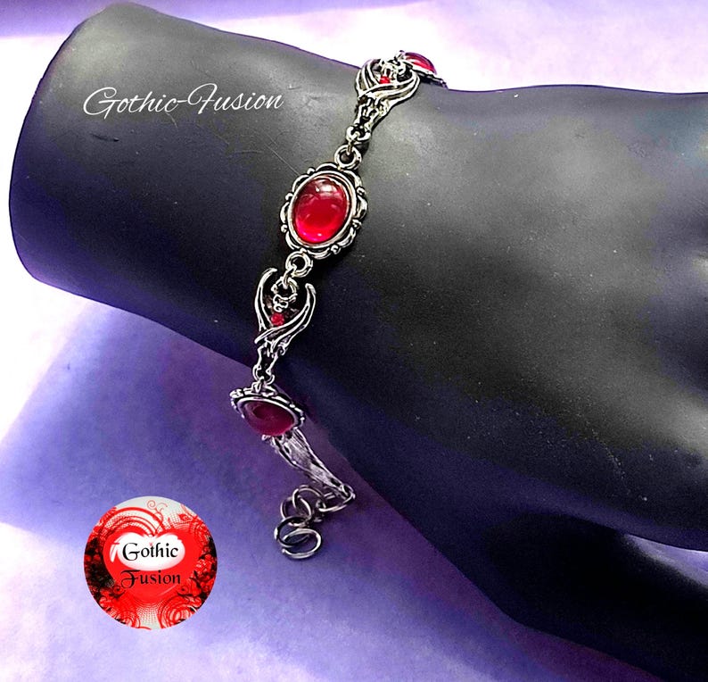 May include: A silver bracelet with a chain link design and red gemstone accents. The bracelet features a delicate, intricate design with a gothic aesthetic.