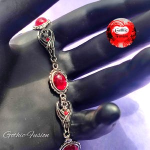 May include: A silver bracelet with red gemstone accents and a bat charm. The bracelet is on a black surface and the text "Gothic Fusion" is visible in the image.