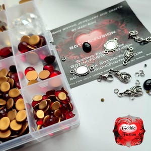 May include: A clear plastic storage box filled with red and gold round glass beads, clear rhinestones, and silver-toned jewelry findings. The box is labeled "Gothic Fusion" and includes a business card with the text "Gothic Fusion Jewelry and Crafts by Jaciann".