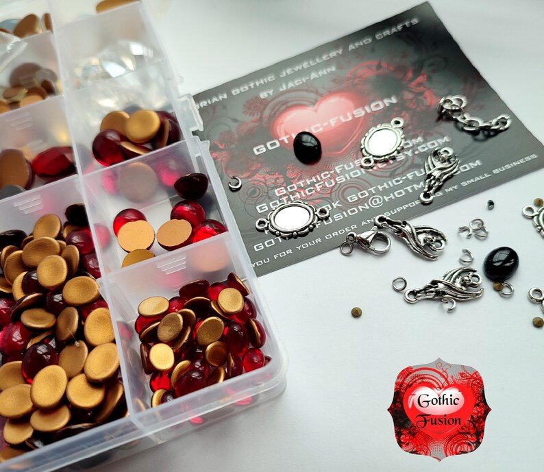 May include: A clear plastic storage box filled with red and gold round glass beads, clear rhinestones, and silver-toned jewelry findings. The box is labeled "Gothic Fusion" and includes a business card with the text "Gothic Fusion Jewelry and Crafts by Jaciann".