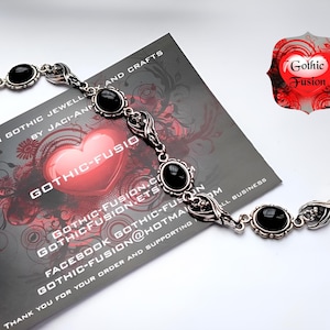 May include: A silver bracelet with black gemstone accents and a delicate, ornate design. The bracelet features a clasp closure and is adorned with intricate details. The bracelet is displayed on a card with the text "Gothic Fusion" and a heart logo.