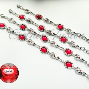 May include: Four silver bracelets with red gemstone accents. Each bracelet features a delicate, ornate design with a repeating pattern of small, silver wings and oval-shaped red gemstones. The bracelets are arranged in a row, with the top bracelet being the shortest and the bottom bracelet being the longest.