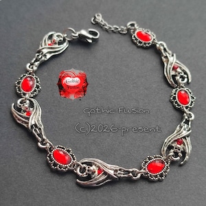 May include: A silver-toned metal bracelet featuring alternating links of stylized bat figures and oval-shaped red faceted stones. The bracelet includes a lobster claw clasp and an extender chain. Text on the image reads Gothic-Fusion (c)2026-present.