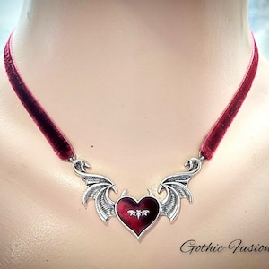 May include: A red velvet choker necklace with a silver pendant featuring a heart with bat wings. The heart is red with a silver bat inside. The text "Gothic-Fusion" is visible in the bottom right corner of the image.