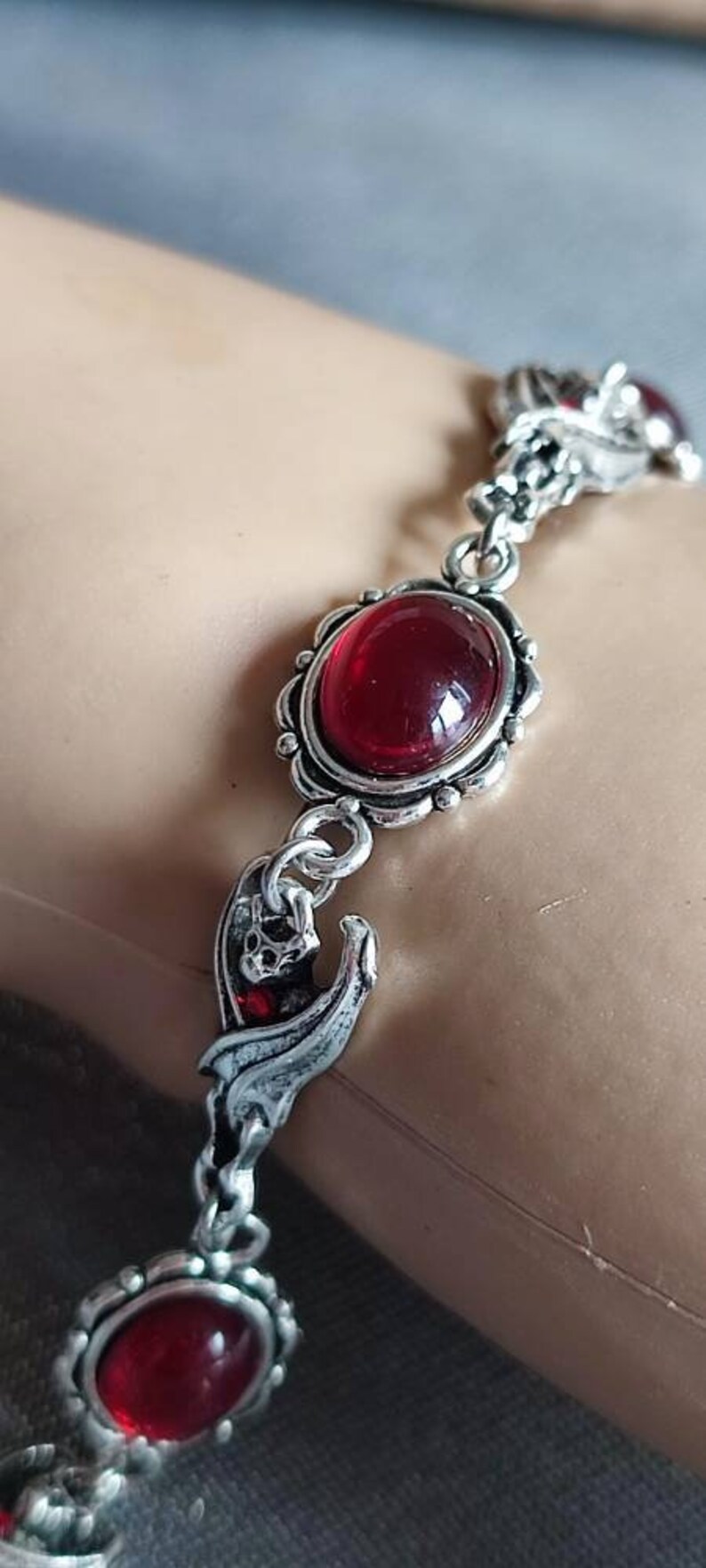 May include: Silver bracelet with red gemstone accents and a bat charm. The bracelet has a delicate chain and ornate detailing.
