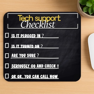 May include: Black rectangular mousepad with the text "Tech support Checklist" in yellow and white. The checklist includes questions like "Is it plugged in?" and "Are you sure?" A computer mouse, keyboard, and a small potted plant are also visible.
