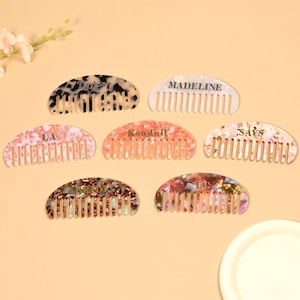 Puede incluir: Colección de seis peines personalizados en varios colores y patrones. Cada peine tiene un diseño único y un nombre impreso, incluyendo "Taylor", "Madeline", "LA", "Kendall", "SAYS" y "LC". Los peines están dispuestos sobre una superficie de color claro.