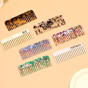 May include: A collection of seven colorful combs with various patterns and colors, including tortoiseshell, speckled, and floral designs. Each comb has a different name or initials printed on it, such as "KM", "RT", "NINON", and "WENDY".