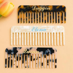 May include: Three personalized combs in the image. The top comb is tortoiseshell with the name "Duggin" in gold script. The middle comb is white with the name "Elena" in blue script. The bottom comb is black and white with the name "Quinn" in gold script.