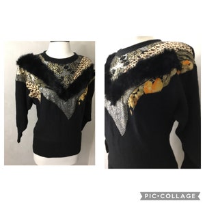 May include: A black sweater with a faux fur collar and a geometric pattern of gold, silver, and brown fabric. The sweater has a round neckline and long sleeves.