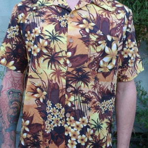 May include: A yellow and brown short-sleeved button-up shirt with a tropical print featuring palm trees and flowers.