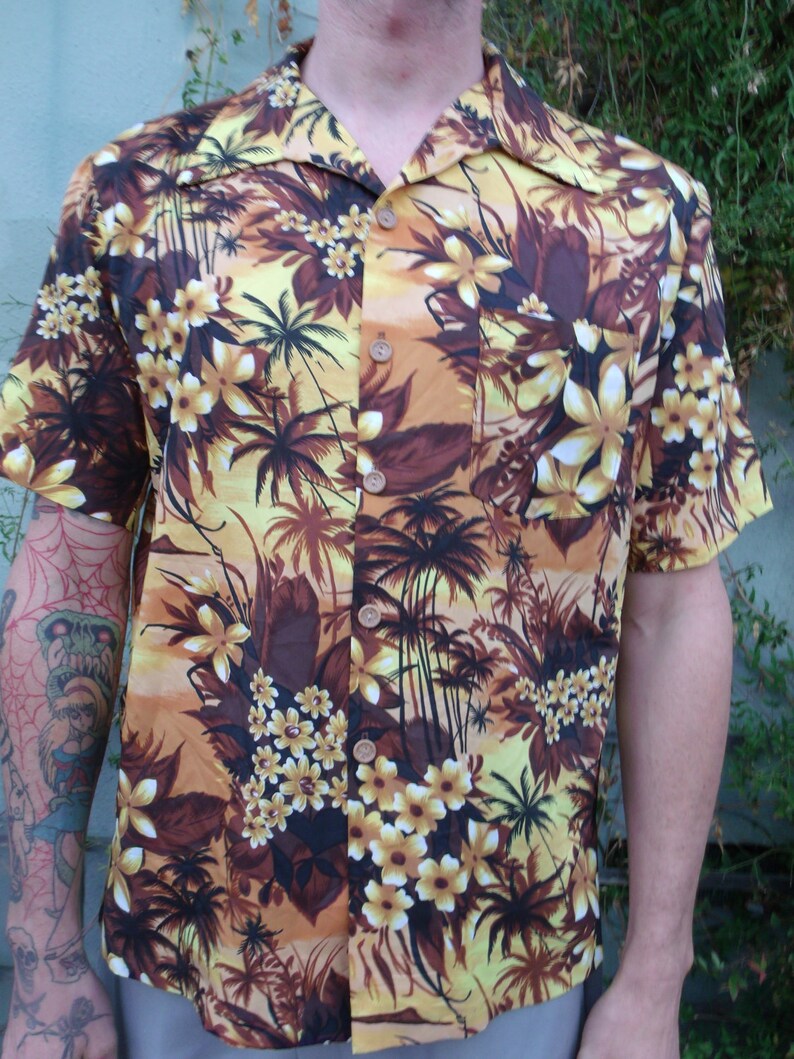 May include: A yellow and brown short-sleeved button-up shirt with a tropical print featuring palm trees and flowers.