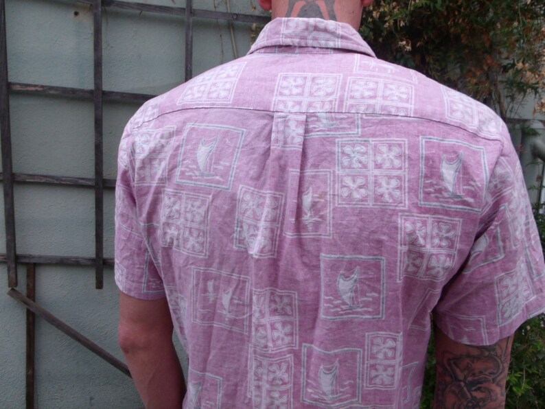 May include: A pink button-down shirt with a white floral pattern. The shirt has a short sleeve and a collared neckline.