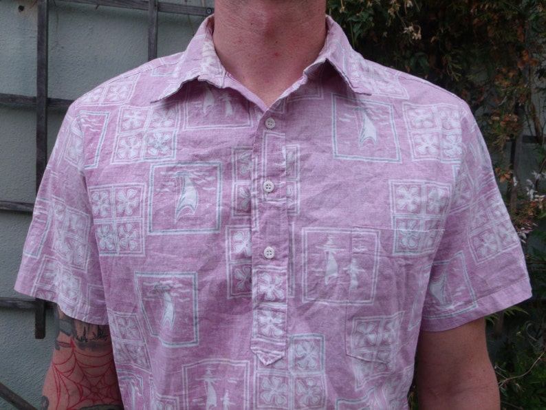 May include: A pink short-sleeved button-down shirt with a white geometric pattern. The shirt has a collar and a button-up front.