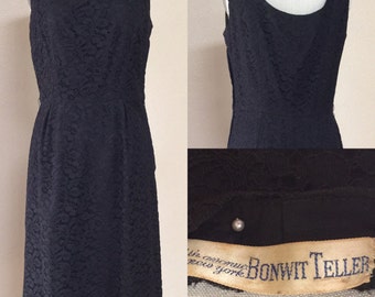 May include: A black sleeveless dress with a lace pattern. The dress has a scoop neckline and a fitted bodice. The dress is labeled "The enormous new york Bonwit Teller".