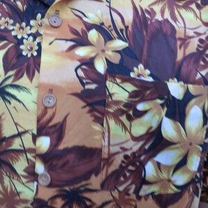 May include: A brown and yellow patterned shirt with a tropical print. The shirt has a button-up collar and a pocket on the left side.