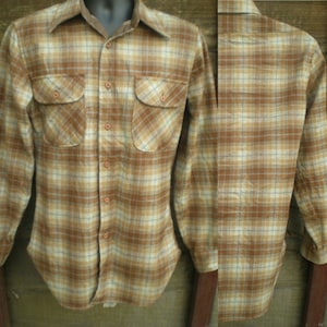 以下が含まれることがあります： 茶色と白のチェック柄の長袖シャツ。胸にポケットが2つ付いています。ボタンダウンカラーで、フロントはボタン留めです。