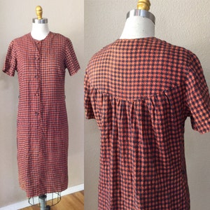 May include: A short-sleeved dress with a button-up front and a gingham pattern in orange and black.