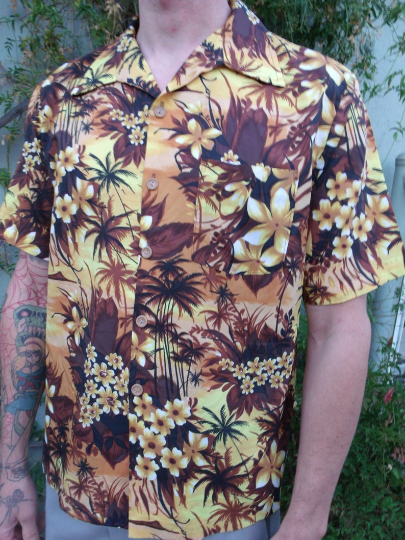 May include: A brown and yellow short-sleeved button-up shirt with a tropical print featuring palm trees and flowers.