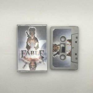 May include: A cassette tape with the title "FABLE" on the cover. The cover art features a young person holding a sword. The cassette tape is silver and has a matching design on the label.