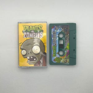 Könnte beinhalten: Eine Plants vs. Zombies-Kassette mit einem gelb-grünen Cover mit einem Zombie-Charakter. Die Kassette ist grün mit einem farbenfrohen Etikett. Der Spieletitel wird sowohl auf der Kassette als auch auf der Hülle angezeigt.