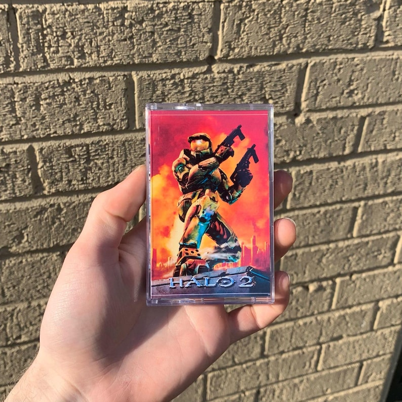 May include: A clear plastic case with a red, orange, and yellow background. The case features a video game character holding two guns. The text "HALO 2" is printed on the case.