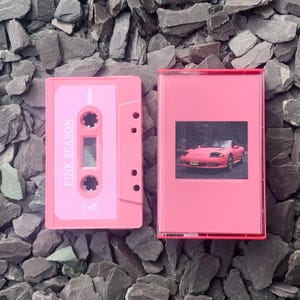 Könnte beinhalten: Rosa Kassette mit dem Text "Pink Season" auf dem Etikett. Die Kassette befindet sich in einem rosa Etui mit einem Foto eines rosa Autos auf der Vorderseite.