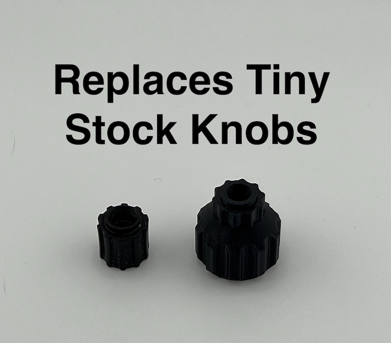 Puede incluir: Dos pomos de pl&aacute;stico negro, uno m&aacute;s grande que el otro. El texto "Reemplaza los pomos peque&ntilde;os de serie" est&aacute; escrito encima de los pomos.