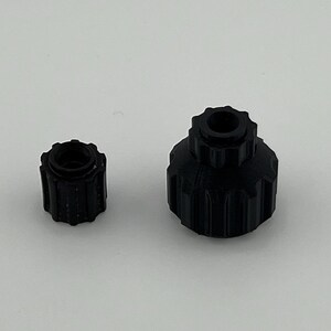 Puede incluir: Dos tapones de botella de pl&aacute;stico negro con un dise&ntilde;o roscado. El tap&oacute;n m&aacute;s grande tiene una abertura m&aacute;s ancha que el m&aacute;s peque&ntilde;o.