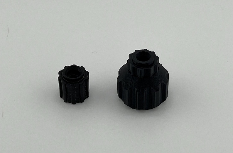 Puede incluir: Dos tapones de botella de pl&aacute;stico negro con un dise&ntilde;o roscado. El tap&oacute;n m&aacute;s grande tiene una abertura m&aacute;s ancha que el m&aacute;s peque&ntilde;o.