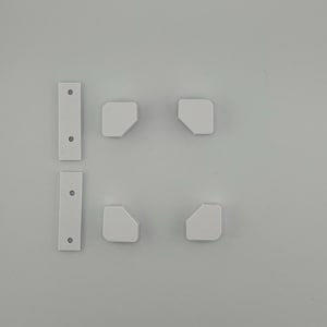 May include: Four white plastic corner brackets and two white plastic strips with holes. The brackets have a rounded edge and the strips have a rectangular shape.