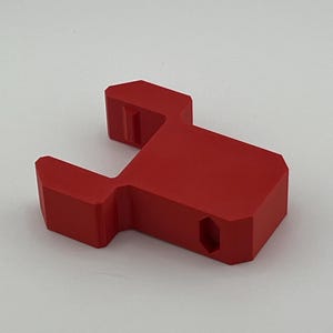 May include: A red plastic 3D printed object with a U-shaped design and a hexagonal hole.