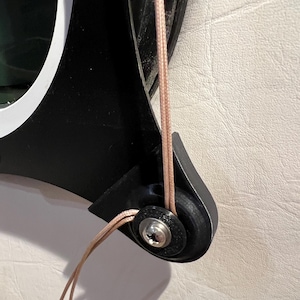 May include: A black and gray round object with a screw and a brown cord attached to it. The cord is looped around the object and tied off.