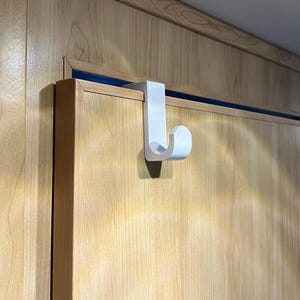 May include: White plastic over-the-door hook for hanging items. The hook is attached to a wooden door.