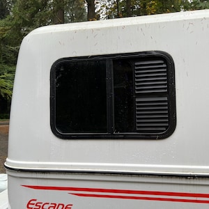 May include: White camper trailer with a black window and a red stripe with the word "Escape" on the side.