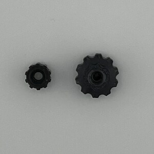 Puede incluir: Dos engranajes de pl&aacute;stico negro, uno m&aacute;s grande que el otro. El engranaje m&aacute;s grande tiene un agujero central y una serie de dientes alrededor del borde. El engranaje m&aacute;s peque&ntilde;o tiene un dise&ntilde;o similar pero es m&aacute;s peque&ntilde;o.