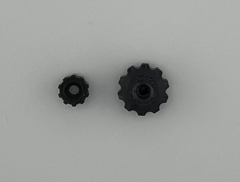 Puede incluir: Dos engranajes de pl&aacute;stico negro, uno m&aacute;s grande que el otro. El engranaje m&aacute;s grande tiene un agujero central y una serie de dientes alrededor del borde. El engranaje m&aacute;s peque&ntilde;o tiene un dise&ntilde;o similar pero es m&aacute;s peque&ntilde;o.