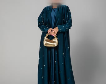 Puede incluir: Una abaya azul turquesa con un bolso de mano dorado. La abaya tiene un patrón sutil de pequeños puntos dorados.