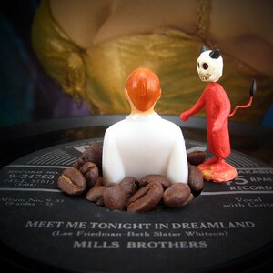 Könnte beinhalten: Eine Vintage-Schallplatte mit einer roten und weißen Teufelsfigur und einer Männerfigur, die auf einem Bett aus Kaffeebohnen sitzt. Das Plattenlabel lautet "Meet Me Tonight in Dreamland (Lee Friedman-Beth Slater Whitson) Mills Brothers" und "Record No. 9-24763 (45-L518) (3:04)".